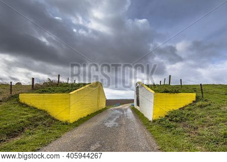 Yellow Painted Road Passage Through Dike At Sunset Under Clouded Sky. Finsterwolde, Oldambt, Groning