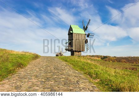 Old Wooden Windmill Covered With Tin-plate On The Hill With Stone Paved Road On A Foreground Against
