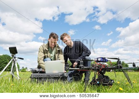 Young male technicians working together on laptop by UAV helicopter and tripod in park