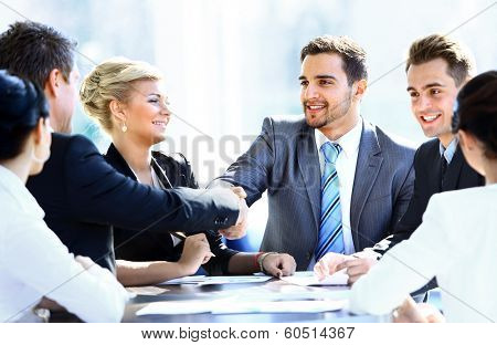 Business colleagues sitting at a table during a meeting with two male executives shaking hands