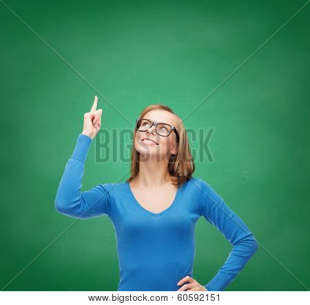 advertisement concept - attractive young woman in casual clothes and black eyeglasses pointing her finger up