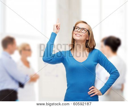 advertisement concept - attractive young woman in casual clothes and black eyeglasses pointing her finger up