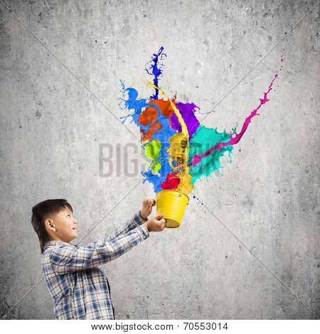 Young boy splashing colorful paint from bucket