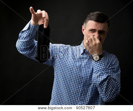 Man holding smelly socks and clogged nose over black background