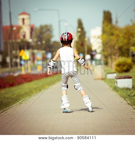 little cute happy girl rollerblading through the city streets. back view