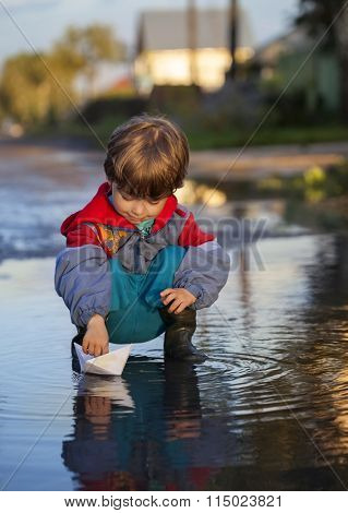 boy play in paper ship in water puddel