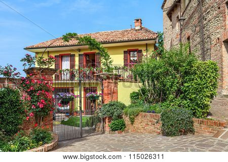 Brick fence with metal gate in front of small yard and typical italian house in Piedmont, Northern Italy.