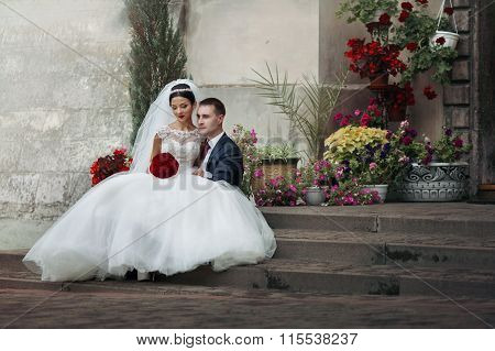 Happy Romantic Valentyne Wedding Couple Sittion On Old Stairs With Flower Plants In The Background