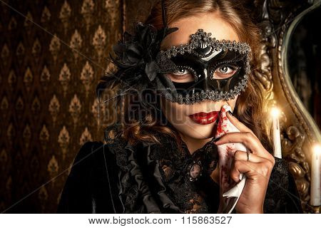 Charming mysterious girl in black mask and black medieval dress stands in a castle living room. Vampire. Halloween concept. Vintage style.