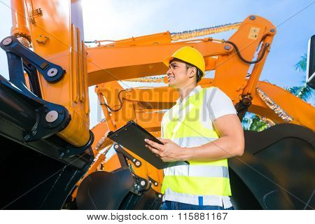 Asian worker controlling construction machinery of building site or mining company