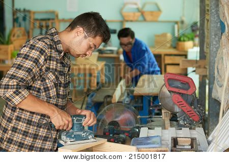 Carpenter in goggles using portable electric planer