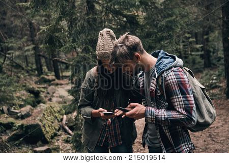 Checking the route. Beautiful young couple using their smart phones while hiking together in the woods