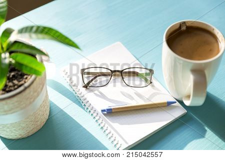 Coffee notebook plant and glases on a blue wooden table on a sunny day