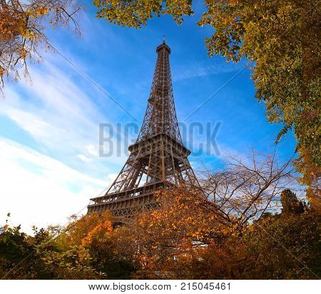Color fall image of the Eiffel tower in Paris, France, Europe, on a sunny autumn day with blue sky and colorful leaves .