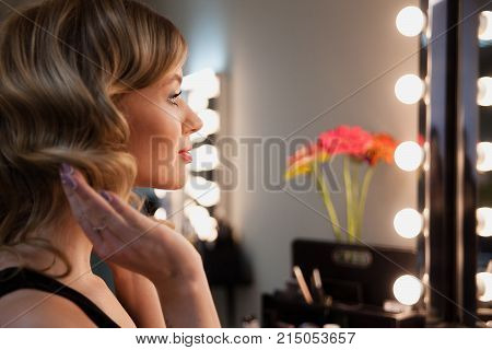 Attractive Blonde Girl Primp At The Mirror With Lamps In The Beauty Studio.