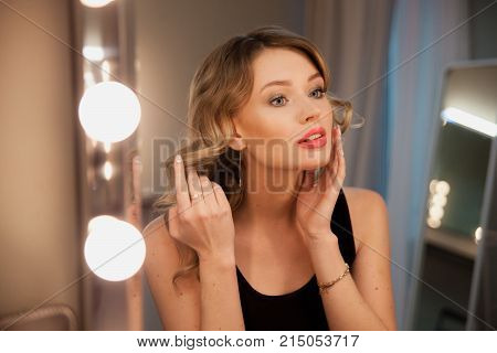 Attractive Blonde Girl Primp At The Mirror With Lamps In The Beauty Studio.