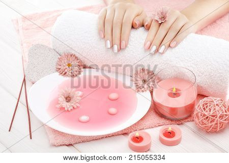 beautiful pinc manicure with candles, chrysanthemum flower and towel on the white wooden table. spa