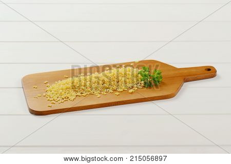 heap of uncooked alphabet pasta on wooden cutting board