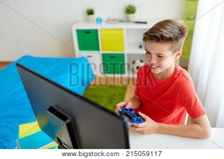 gaming, technology and people concept - smiling boy with gamepad and computer playing video game at home