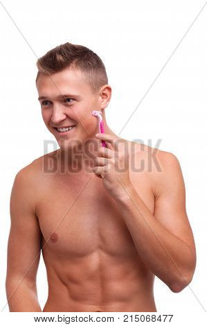 A guy with a naked torso, with a happy face shaves his cheeks with a pink razor on a white isolated background