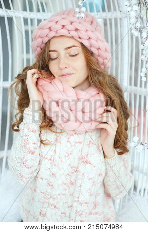 Young woman sitting on the bench wearing thick knitted pink wool hat and snood. Winter outfit.