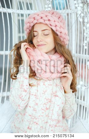 Young woman sitting on the bench wearing thick knitted pink wool hat and snood. Winter outfit.