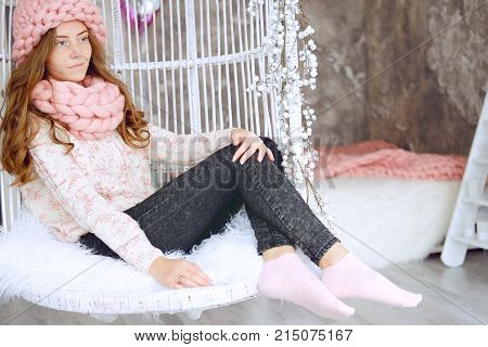 Young woman with red hair and dressed in sweater and knitted pink hat and snood sitting in her favourite chair