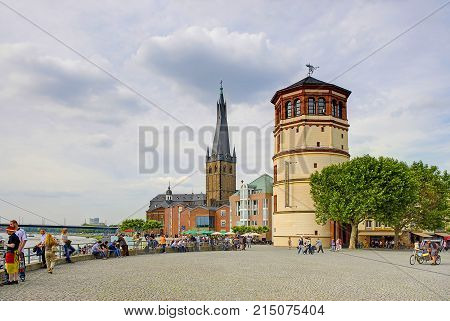DUSSELDORF, GERMANY, JUN.13, 2010: View on city riverwalk with people, roman cathedral church and tower. People and tourists on open city square along riverwalk. Classical european architecture