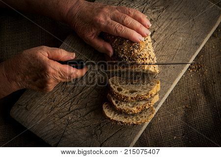Woman's hands slicing homemade wheat bread on wooden cutting board.