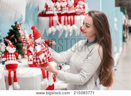 Cheerful happy customer girl choosing gifts for Christmas and New Year. She is holding snowman toys