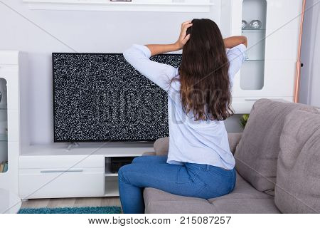 Rear View Of A Woman On Sofa Getting Frustrated With Glitch TV Screen At Home