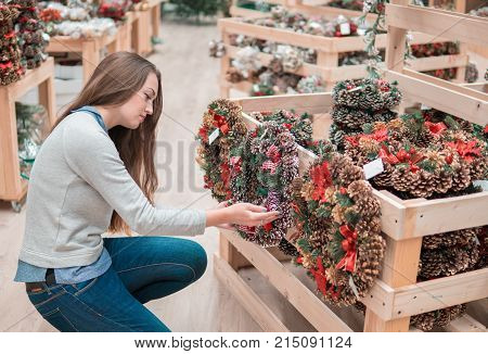 customer girl choosing Christmas decorations. difficult decision. Various choice of New Year's wreath with decorations