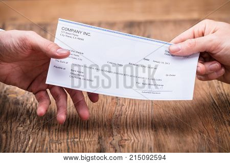 Close-up Of Businessperson's Hand Giving Cheque To Partner Over Wooden Desk