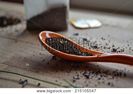 Tea dust and tea granules in the orange spoon at wooden background