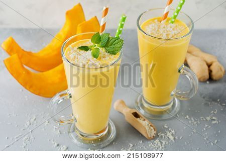 Pumpkin smoothies with ginger and coconut shavings and mint in a glass on light stone or concrete background. Healthy and delicious drink for breakfast. Selective focus. Top view. Copy space.