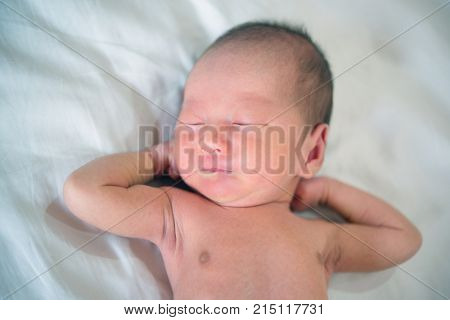 Newborn baby boy lies on bed and stretches, 7 days old.