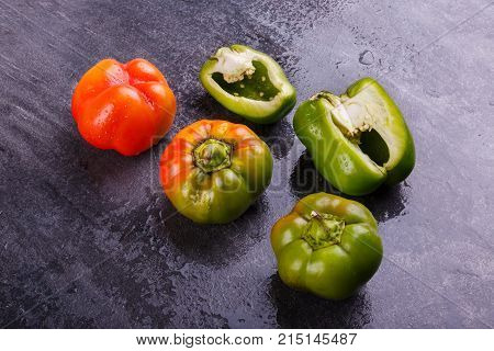 Appetizing, juicy, Bulgarian pepper, cut in half, and whole, orange and green, on a black background