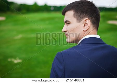 Portrait in profile of handsome, thoughtfull asian groom in a dark blue against the backdrop of green meadow. concept of a strong successful man