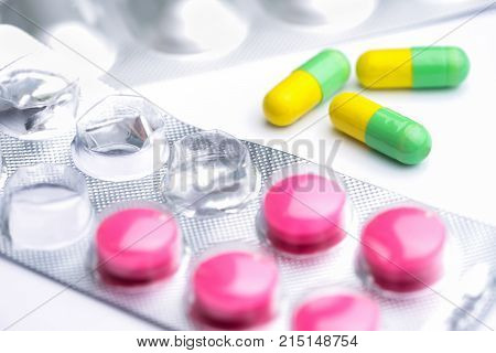 Yellow and green capsule with used magenta tablets medical pills in silver foil pack on white background.