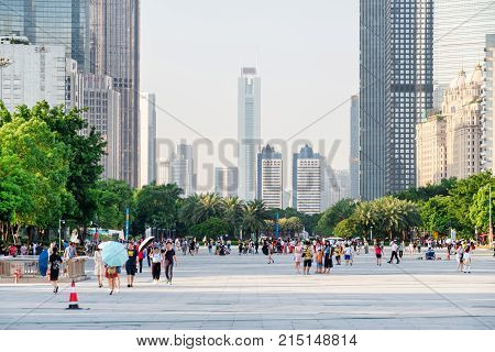 Asian Tourists Walking In A City Park Among Modern Buildings