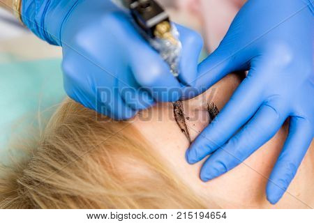 Cosmetologist applying permanent make up on eyebrows. Beautiful woman with smooth young skin sitting in a beautician. A beautician performs modeling permanent eyebrows makings.