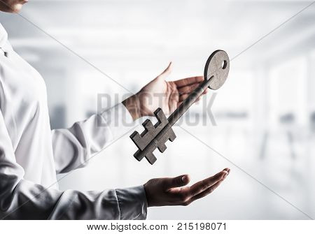 Business woman in white shirt keeping big stone key in hands with office view on background. Mixed media.