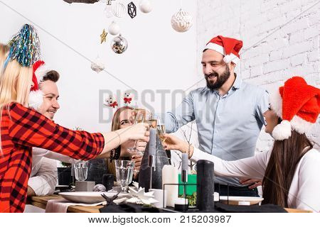 Christmas party cheerful friends at having drink and fun. Men and women at a festive table with glasses of champagne in a white room