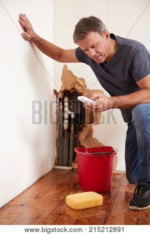 Middle aged man with a burst pipe dialling phone for help