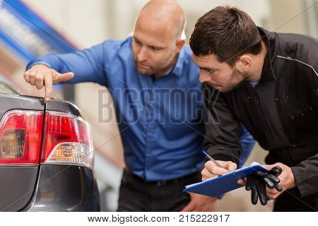 auto service, repair, maintenance and people concept - mechanic with clipboard and customer or car owner looking at taillight at workshop