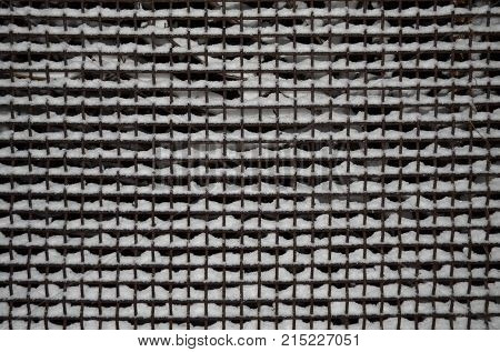 The cells of the metal grid are covered with a layer of snow.