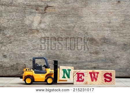 Yellow plastic forklift hold letter N to complete word news on wood background