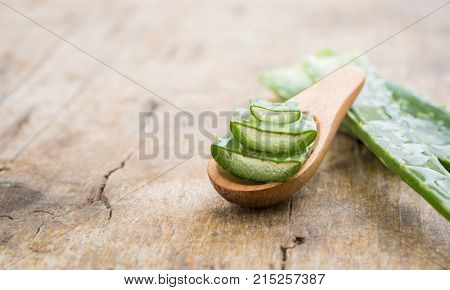 Closeup with copy space of slices of aloe vera on wodeen spoon. Detail of wet leaves of aloe on wooden background. Beauty and spa treatment concept. 