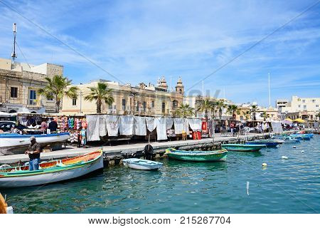 MARSAXLOKK, MALTA - APRIL 1, 2017 - Traditional Maltese Dghajsa fishing boats in the harbour with waterfront buildings and market stalls to the rear Marsaxlokk Malta Europe, April 1, 2017.