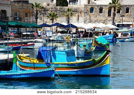 MARSAXLOKK, MALTA - APRIL 1, 2017 - Traditional Maltese Dghajsa fishing boats in the harbour with waterfront buildings and restaurants to the rear Marsaxlokk Malta Europe, April 1, 2017.